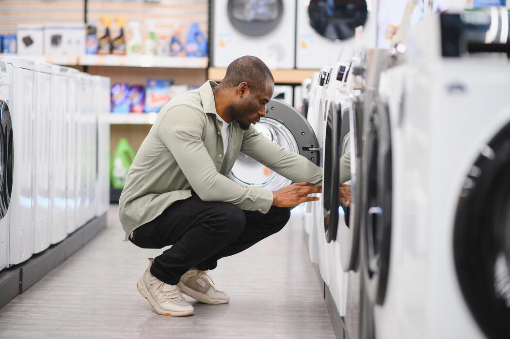 Man examining front-loading washing machines in an appliance store