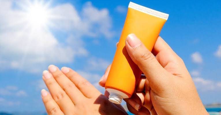 Hands applying sunscreen under bright sunlight with blue sky background