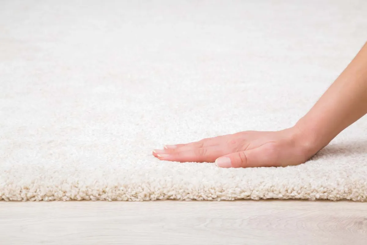 Hand touching a soft white carpet to show its texture and thickness.