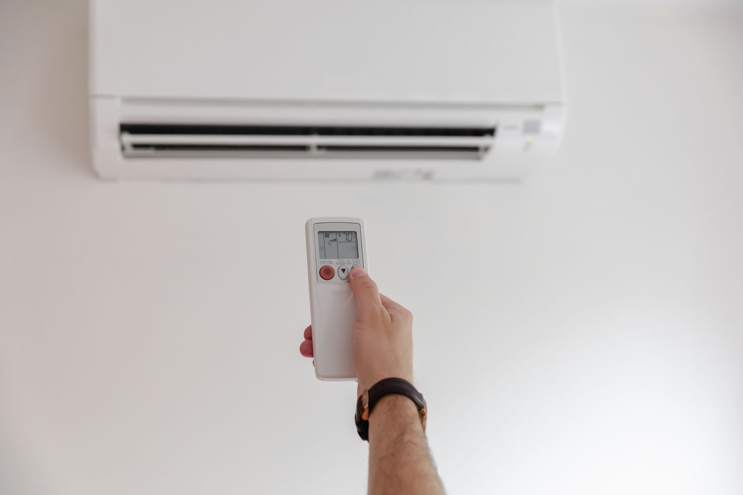 Hand using a remote control to adjust a wall-mounted air conditioner