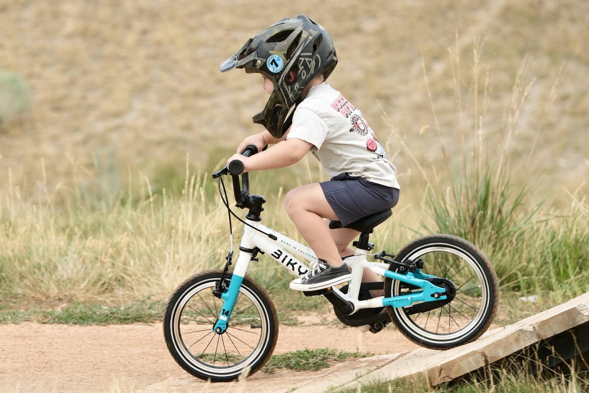 Child wearing a helmet riding a small balance bike on an outdoor trail.