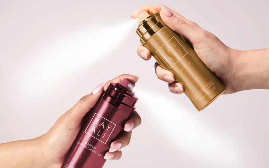 Hands holding body spray bottles with fragrance mist being sprayed on a white background
