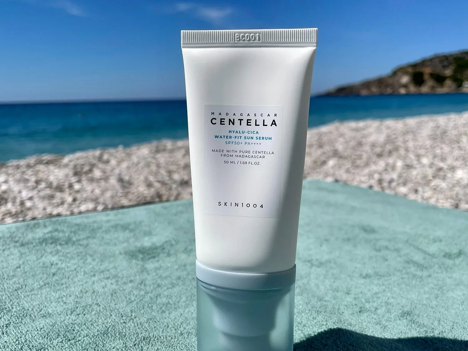 Sunscreen tube displayed on a beach with ocean and blue sky background
