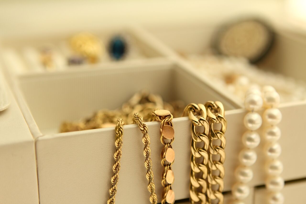 Gold chains and pearl jewelry arranged inside an open cream-colored jewelry box.
