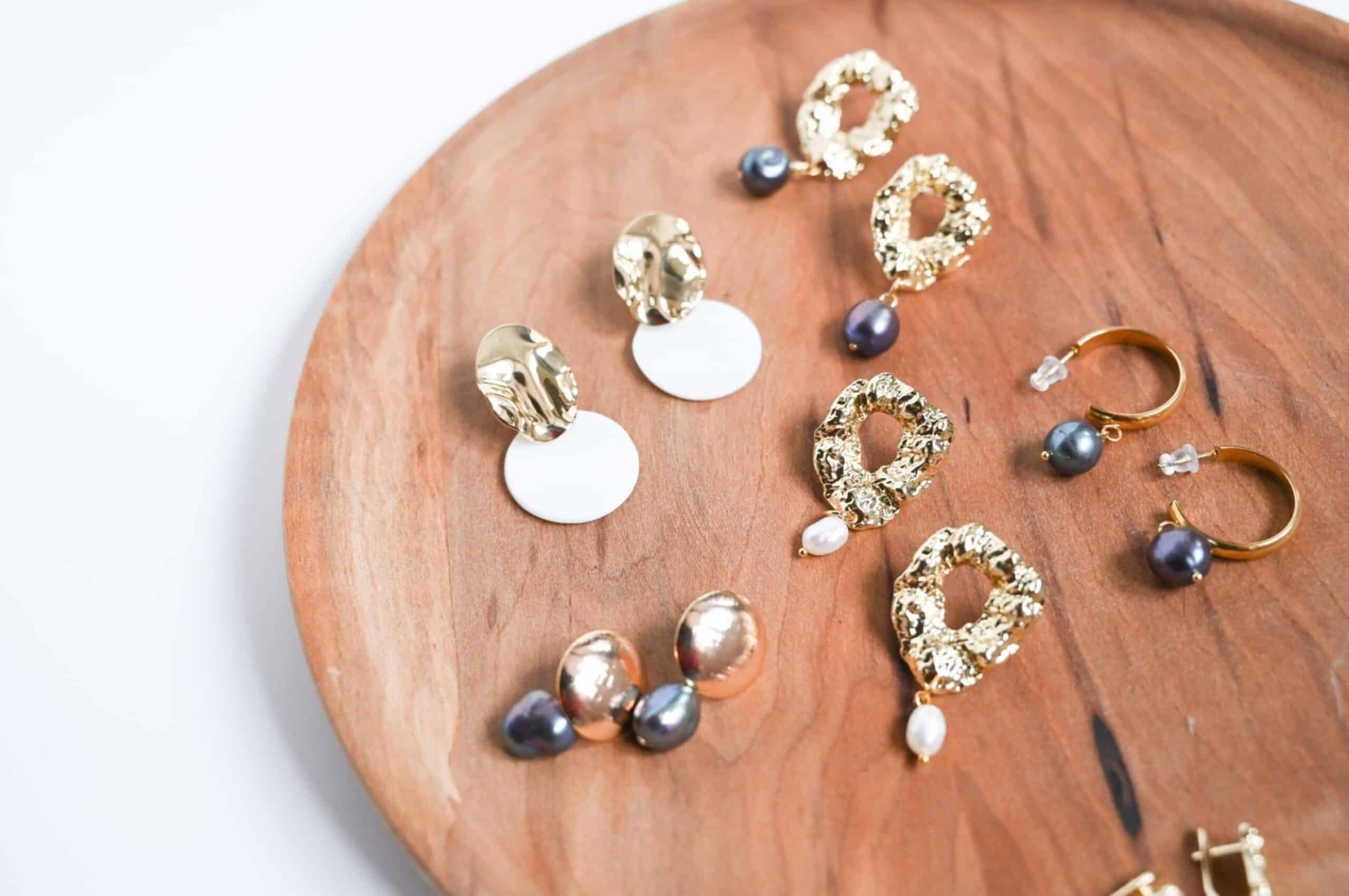 Assorted gold and pearl earrings arranged on a round wooden tray.
