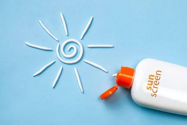 Sunscreen bottle with cream forming a sun symbol on blue background