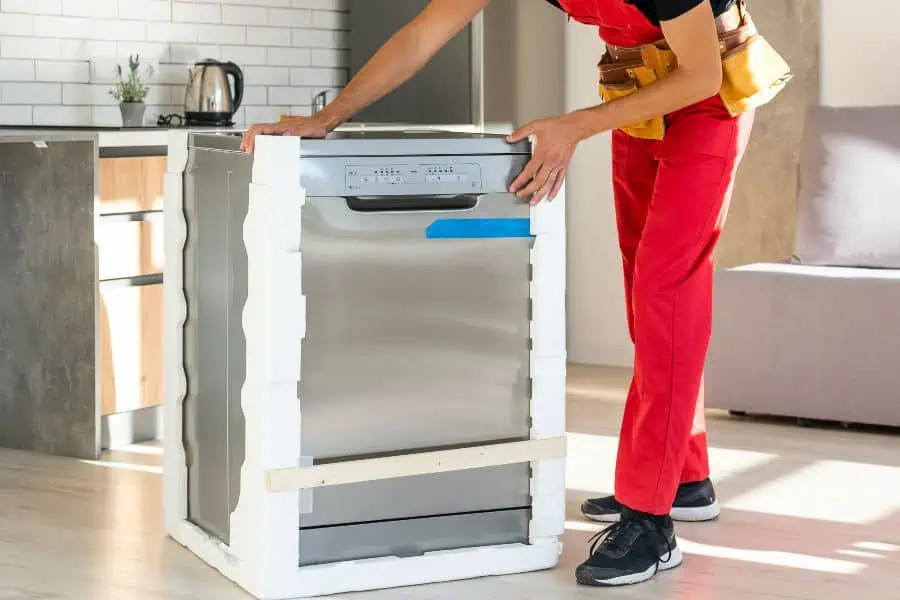 Technician unpacking and inspecting a new dishwasher in a modern kitchen