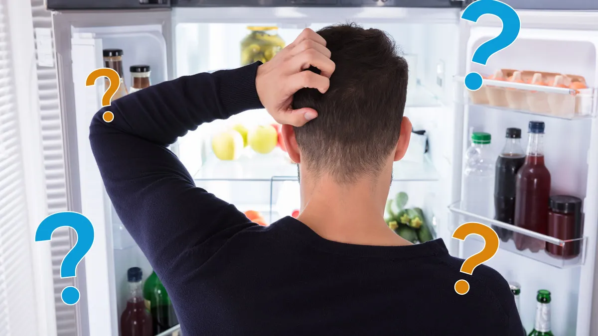 Man looking confused inside an open refrigerator with question marks around him.