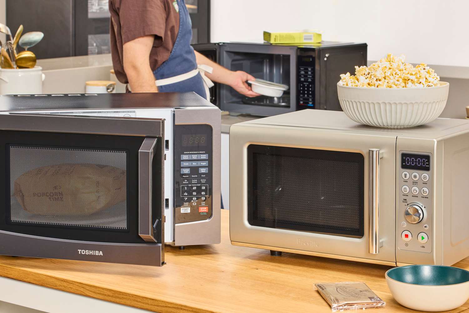 Two microwave ovens displayed on a kitchen counter with a bowl of popcorn.