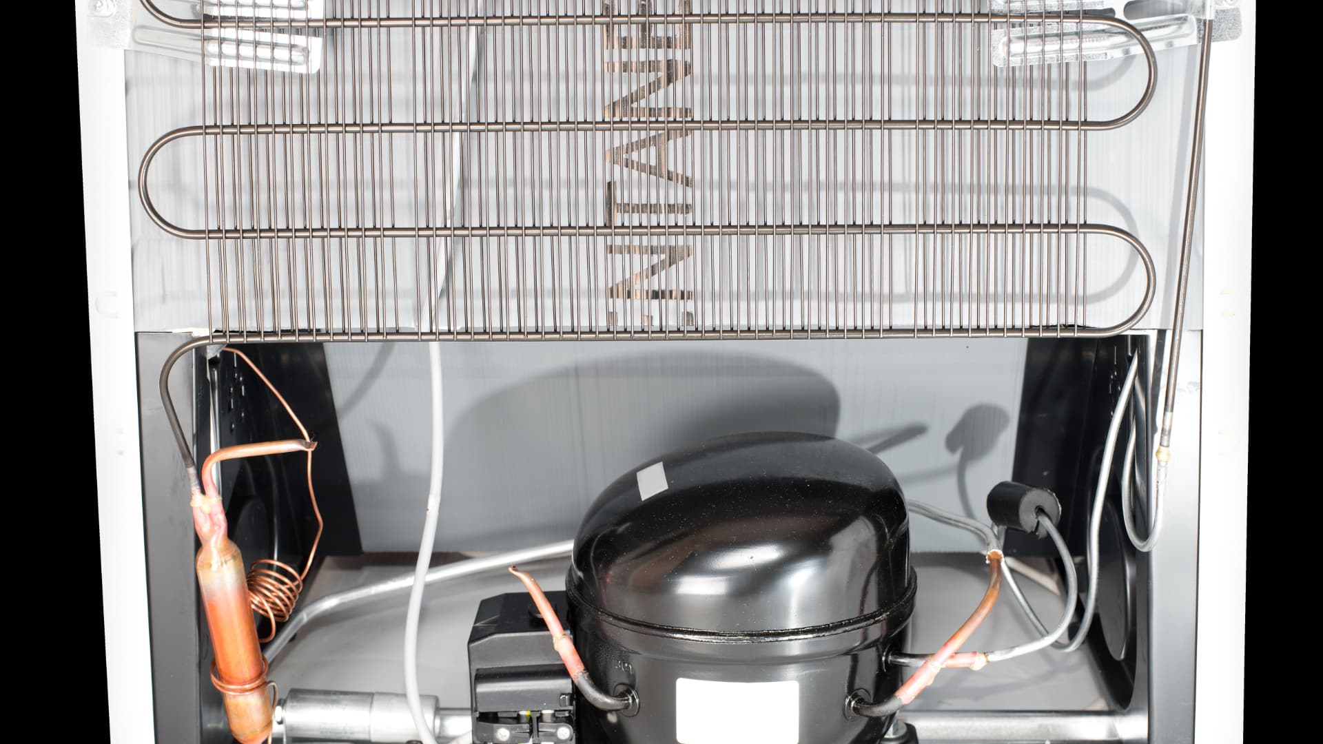 Rear view of a refrigerator compressor, condenser coils, and cooling system components.