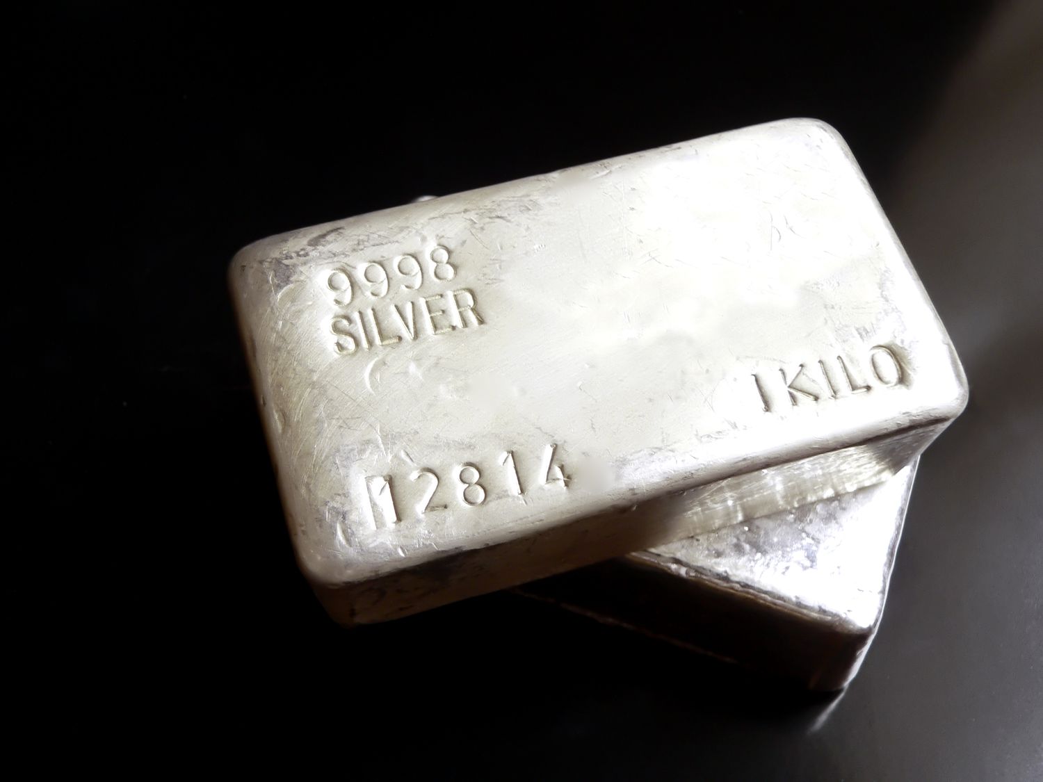 Two one-kilogram 999.8 fine silver bars stacked on a black surface