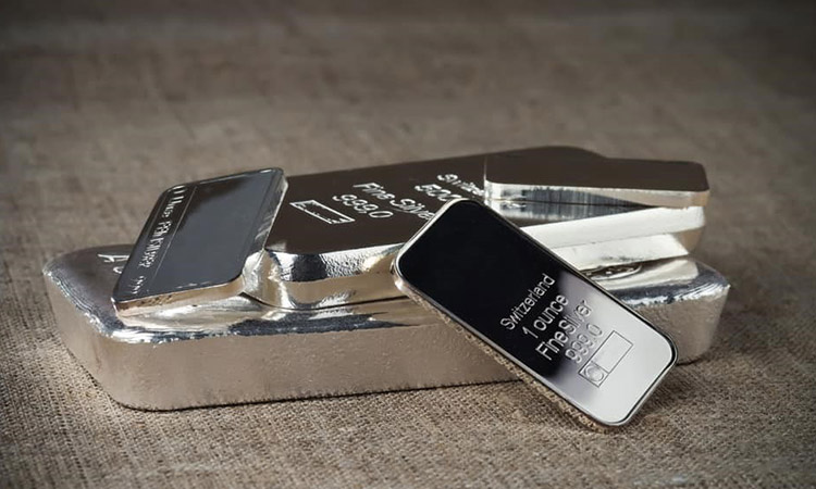 Stacked silver bars of different sizes displayed on a textured surface