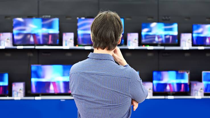 Customer comparing multiple televisions displayed in an electronics store 