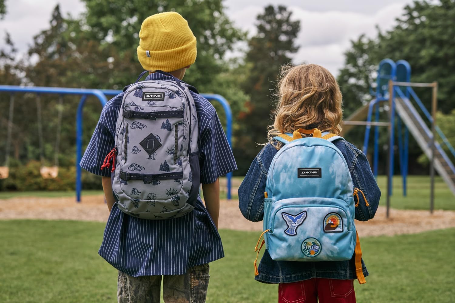 Two children wearing colorful school backpacks at a playground