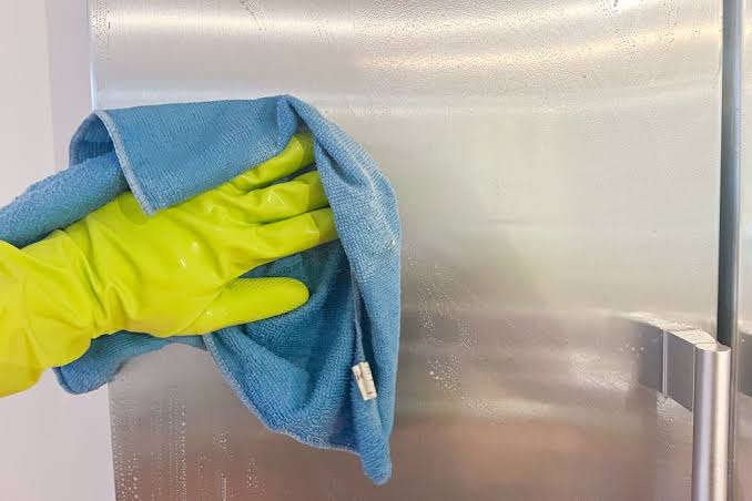 Cleaning a stainless steel refrigerator door with a microfiber cloth and gloves