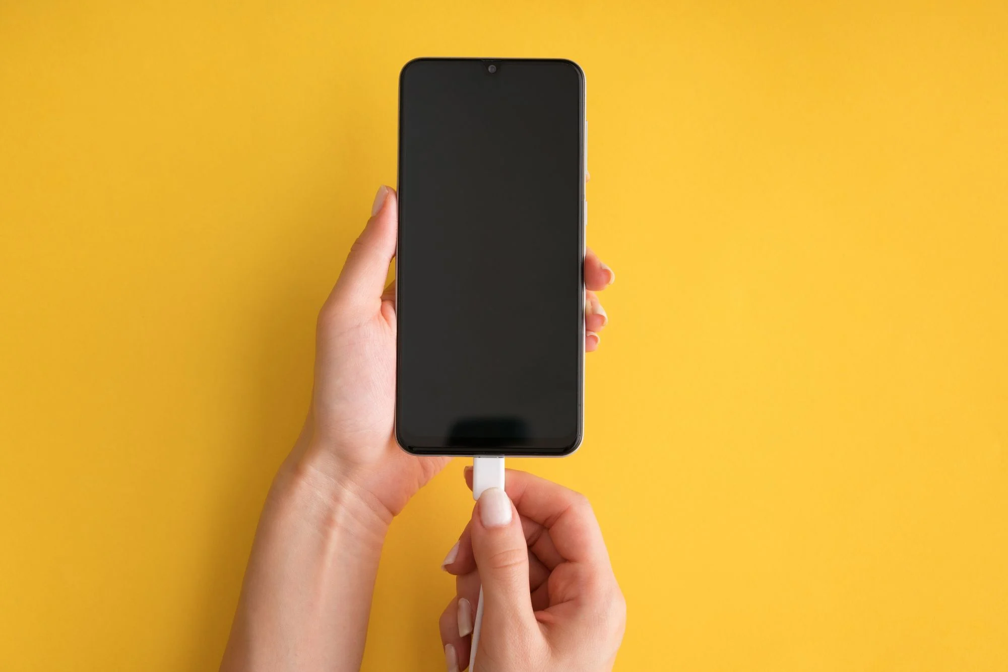 Connecting a charging cable to a smartphone on a yellow background
