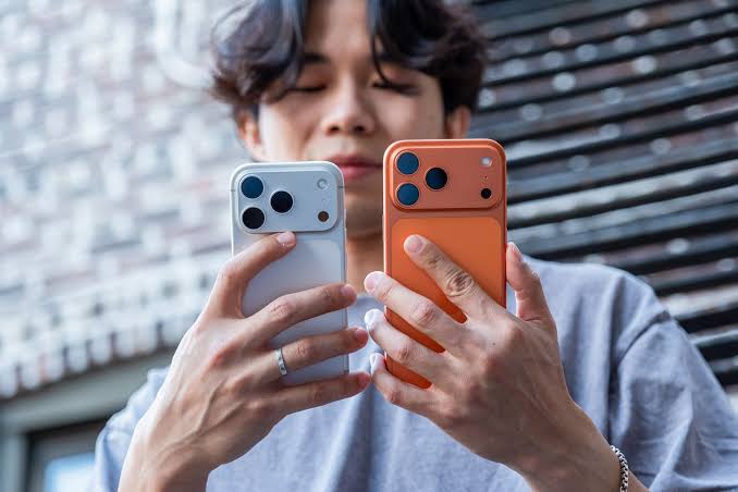 Person holding silver and orange iPhone Pro models side by side