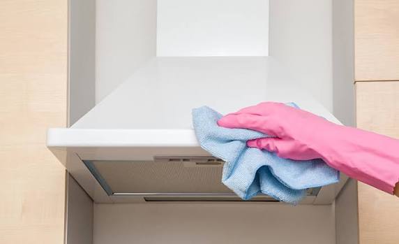 Cleaning a white kitchen range hood with a microfiber cloth and gloves