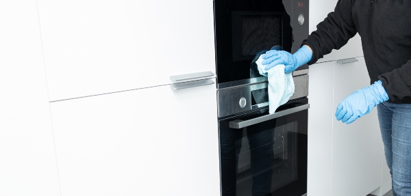 Cleaning a built-in oven with a microfiber cloth and protective gloves