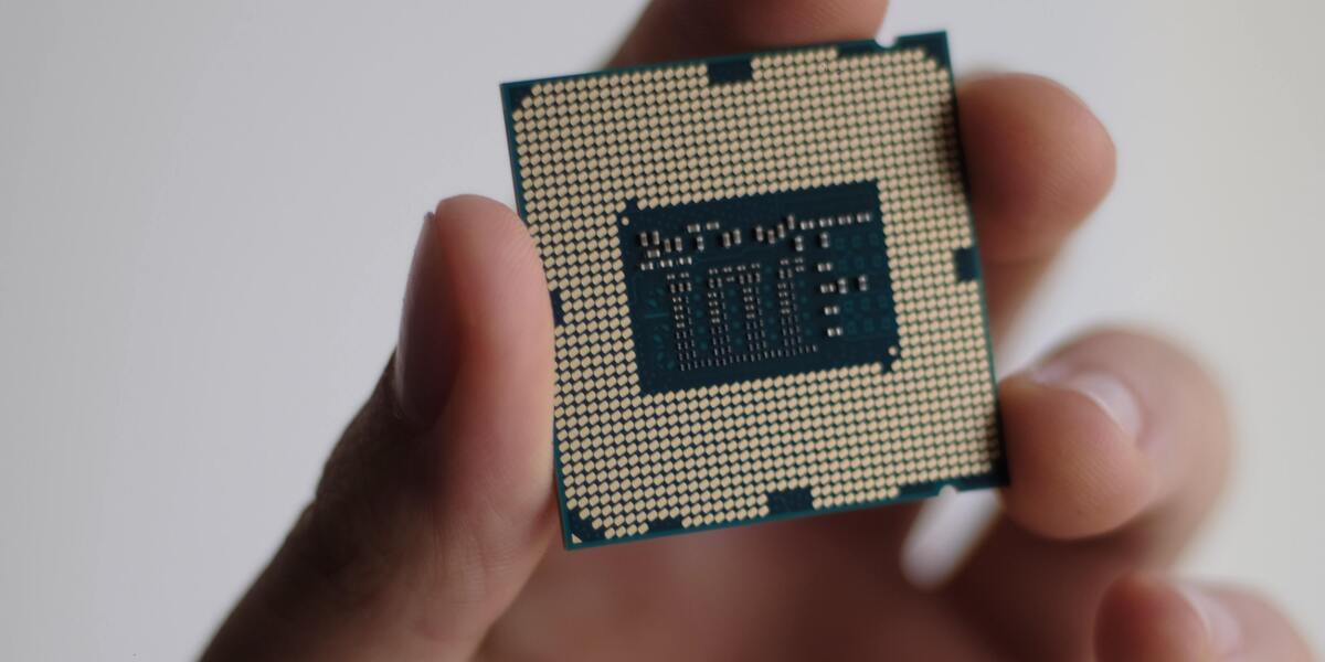 Computer processor chip held between fingers showing underside contact pins