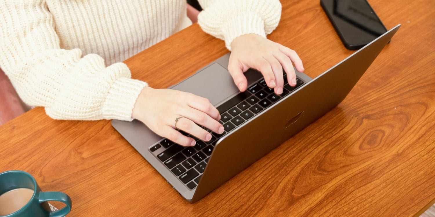 Person typing on a laptop at a wooden desk