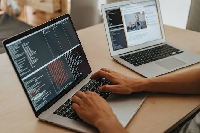 Developer coding on a laptop with a second laptop in the background