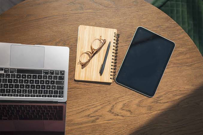 Laptop, tablet, notebook, and glasses on a wooden desk