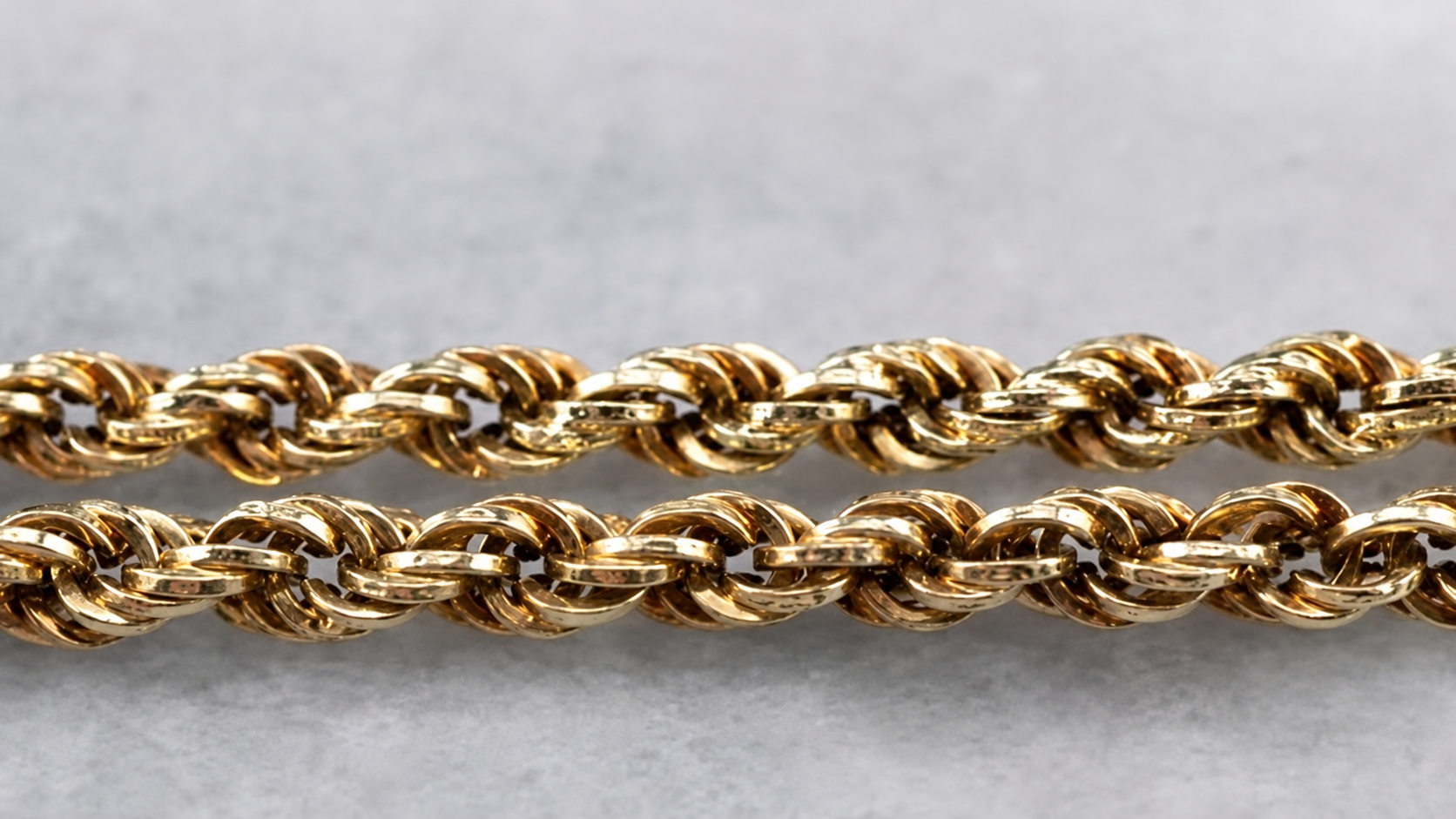 Close-up of two parallel gold rope chains on a gray background
