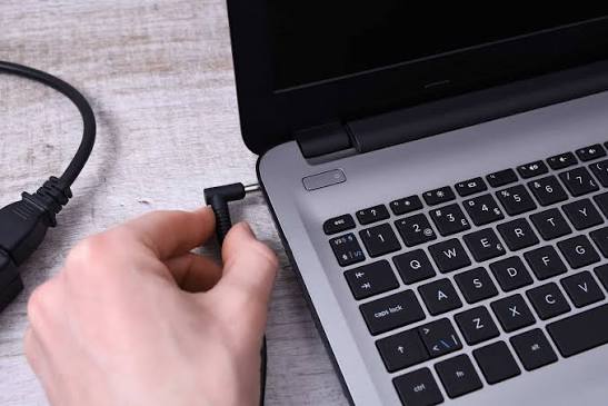 Hand plugging a charging cable into a laptop for proper battery charging