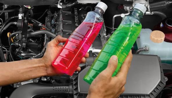 Red and green antifreeze coolant bottles held over a car engine bay