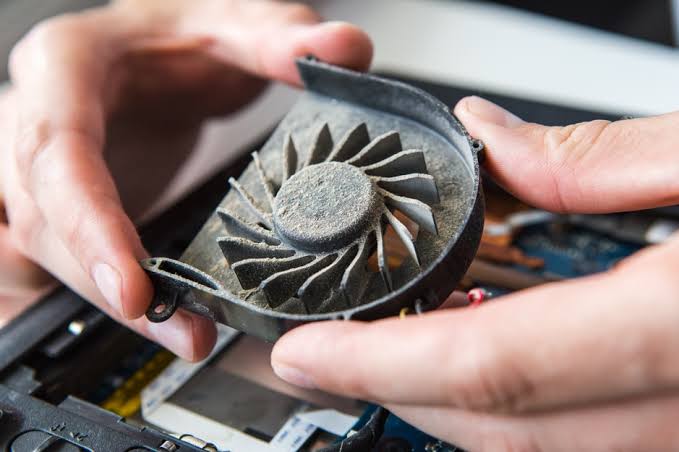 Dusty laptop cooling fan being removed for cleaning