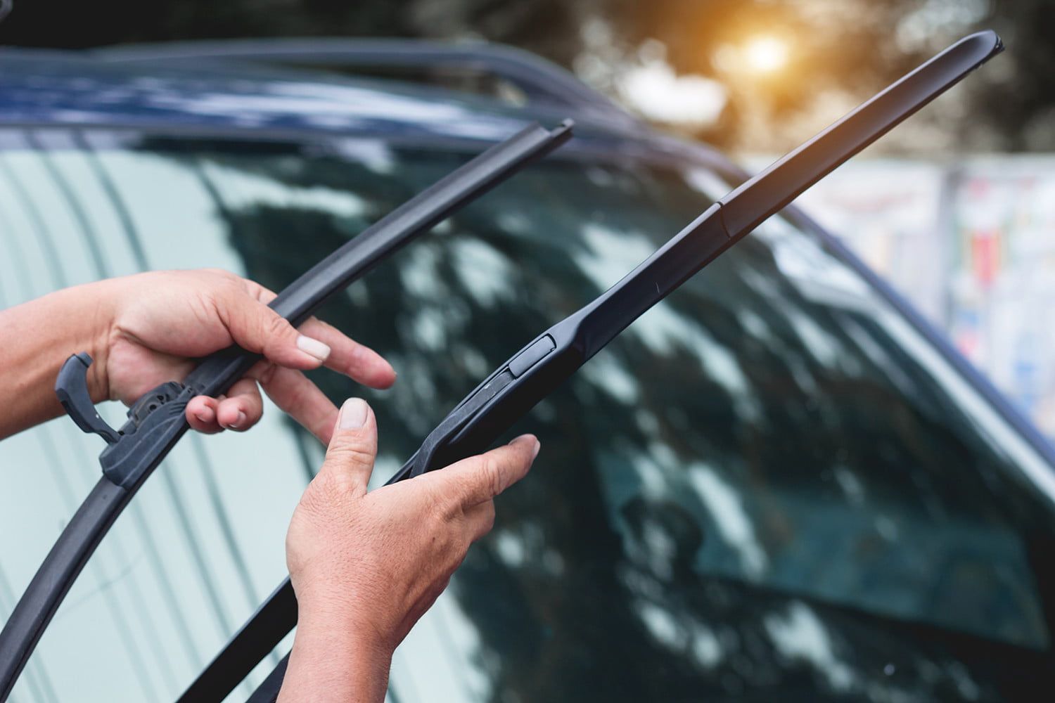 Hands inspecting car windshield wiper blades before replacement.
